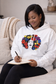 Black woman  wearing a white floral portrait hoodie while journaling on a cozy beige couch in a softly lit living room