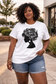 Confident Black woman in her 40s styled in beige shorts and white cotton tee featuring black floral afro profile artwork.